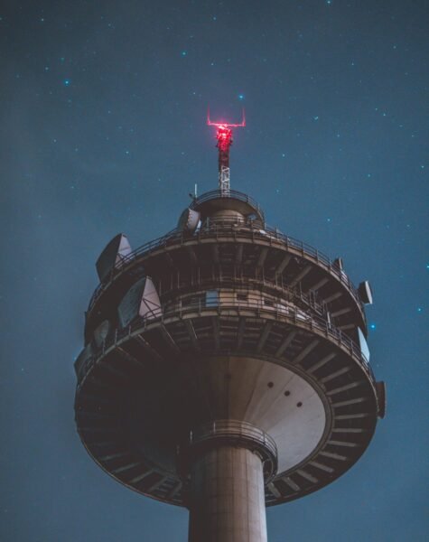 Vertical low angle shot of a grey tall tower at night with beautiful stars in the background A vertical low angle shot of a grey tall tower at night with beautiful stars in the background